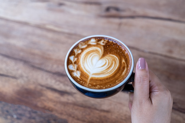 コーヒーショップカフェで女性の手にコーヒーカフェラテアートのカップのクローズアップ