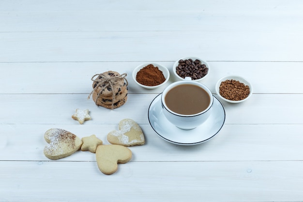 Чашка кофе крупным планом с кофейными зернами, растворимым кофе, какао, различными видами печенья на фоне белой деревянной доски. горизонтальный
