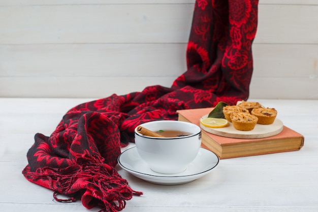 Close-up of cup of tea, white cookies in a plate with red scarf and a book