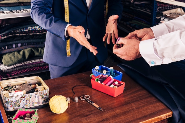 Close-up of customer's hand showing thread spool to male tailor in shop