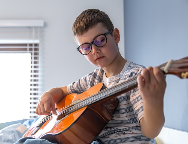 Chiuda sul ragazzo carino con gli occhiali impara a suonare la chitarra classica a casa.