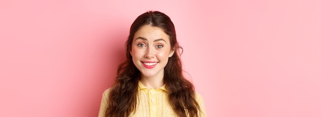 Free photo close up of cute brunette lady smiles at camera trying to make friendly and polite face stands again