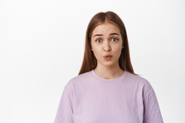 Close up of cute girl pucker lips and looking silly, makes clingy coy face, asking for smth, begging, say please, standing in t-shirt against white background. Copy space