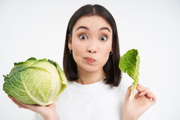 Close up of cute korean woman eating cabbage on diet holding lettuce isolated on white background