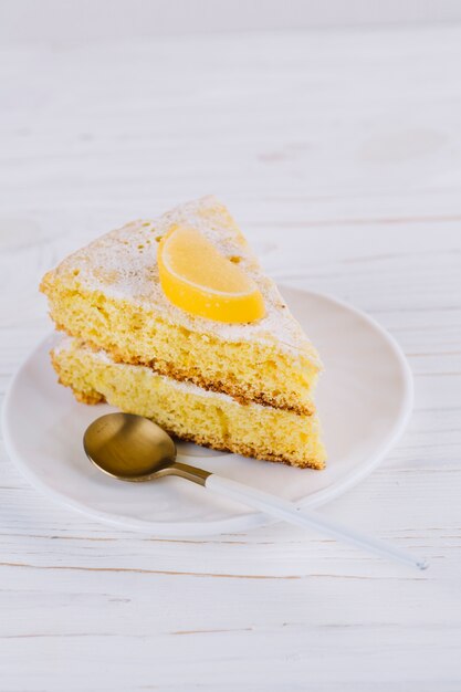 Close-up of a decorated lemon cake slice in white plate with spoon