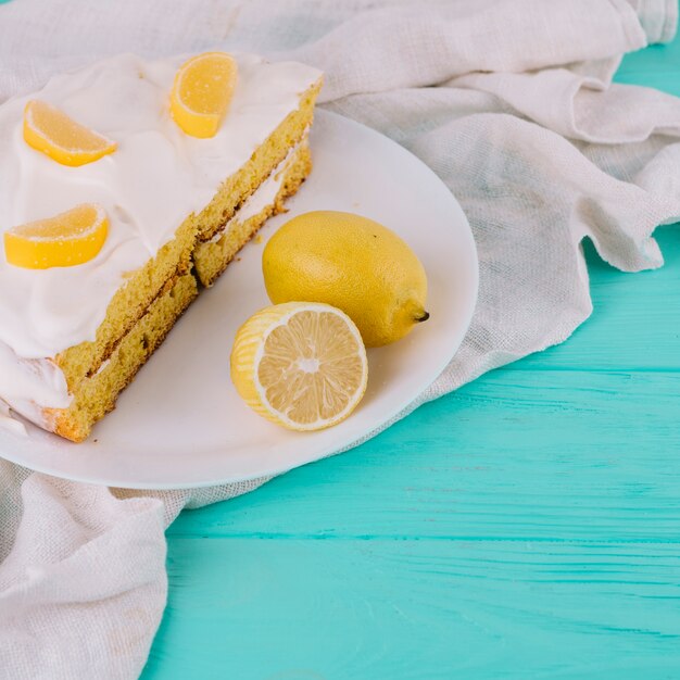 Close-up of a decorated lemon cake in white plate with lemons on wooden table