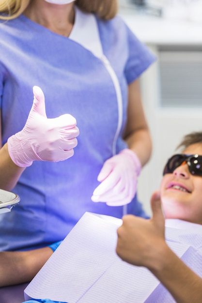 Foto gratuita primo piano della mano di un ragazzo e del dentista che gesturing i pollici su