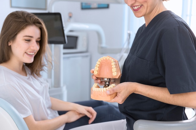 웃는 환자에게 치아 모델을 보여주는 치과 의사의 근접