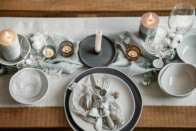 Закройте деталь сервировки праздничного стола с набором столовых приборов, тарелки и свечей в подсвечниках.