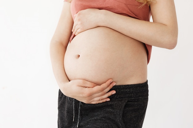 Close up detail of young beautiful mother holding her pregnant belly with hands