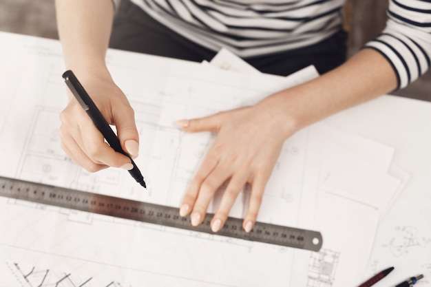 Free photo close up detail of young successful engineer girl in striped top and black jeans, making work at home, working on new blueprint with hand and gun