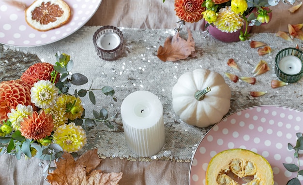Детали декора праздничного осеннего стола крупным планом, цветы, свечи и тыквы.