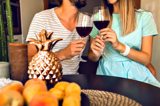 Close up details of romantic evening of pretty couple drinking red wine end enjoying time together, modern interior and trendy elegant clothes.