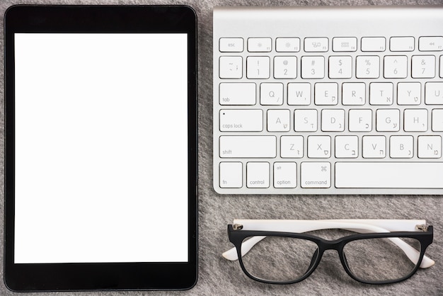 Free photo close-up of digital tablet with white screen display; wireless keyboard and eyeglasses on desk