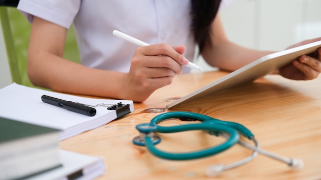 컴퓨터 태블릿을 사용하는 동안 의료 보고서를 검토하는 의사를 닫습니다.