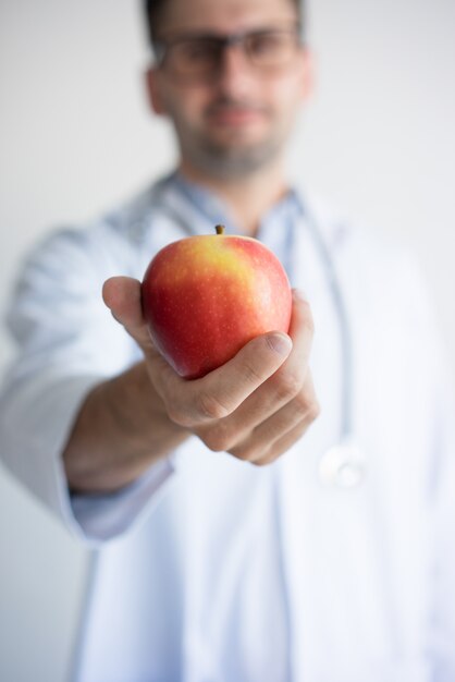 Close-up of doctor hand giving red apple. Young Caucasian male dentist 