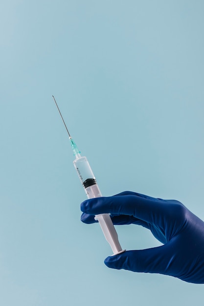 close-up of a doctor hand with syringe on blue backdrop