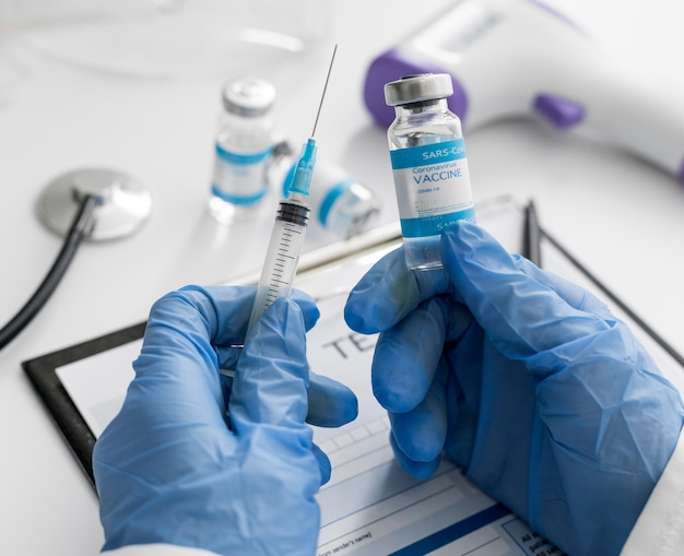 Close-up doctor holding covid vaccine and syringe