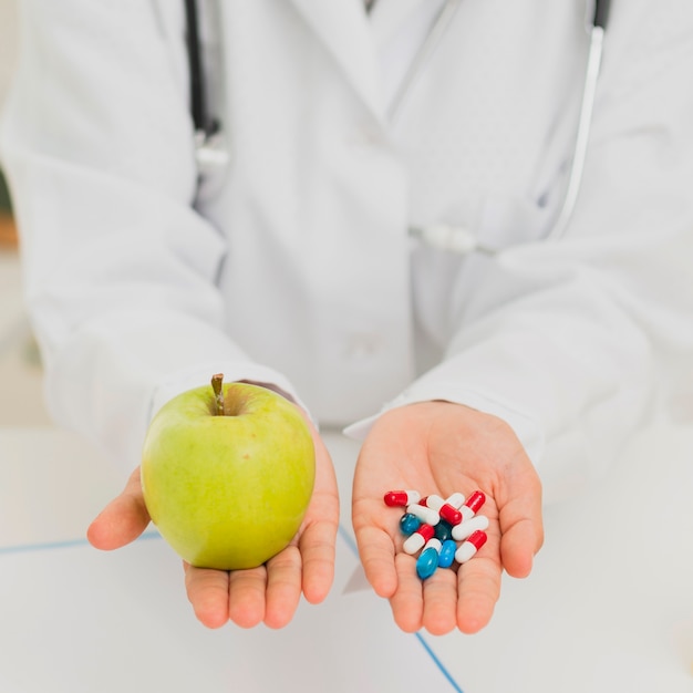 Close-up doctor holding green apple and pills