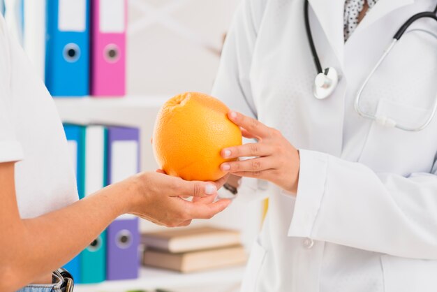 Close-up doctor and patient holding an orange