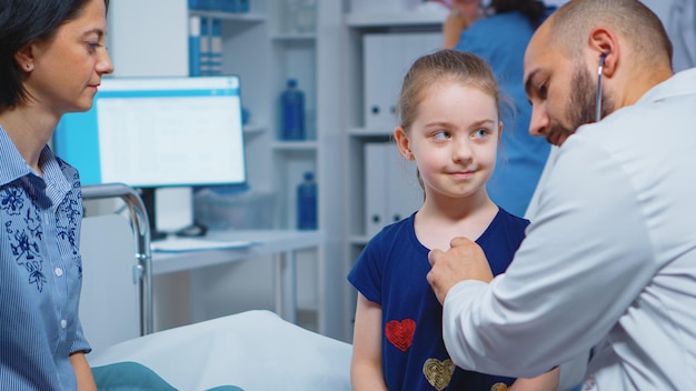 Close up of doctor using stethoscope for listening child heartbeat. Healthcare practitioner physician specialist in medicine providing health care services consultation treatment in hospital cabinet