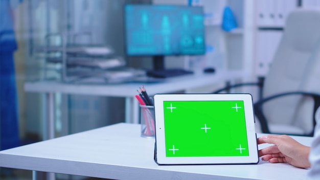 병원 캐비닛에 녹색 크로마 키가 있는 태블릿 컴퓨터를 사용하는 의사의 클로즈업. 의학 연구를 하는 교체 가능한 화면으로 태블릿 컴퓨터에서 작업하는 건강 클리닉의 의사.