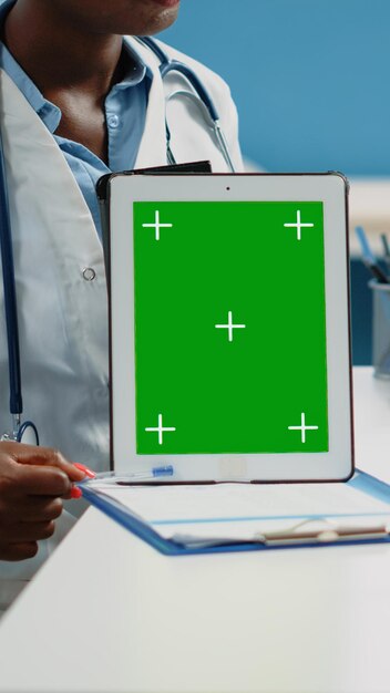 Close up of doctor vertically holding tablet with green screen on desk. Medical specialist showing mockup isolated template and background for chroma key on digital gadget in cabinet