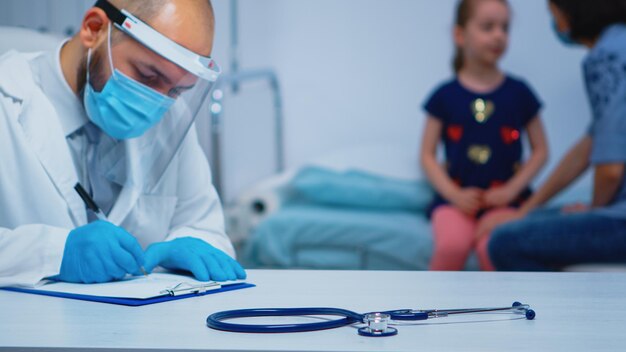 Close up of doctor wearing protective mask and gloves writing medical treatment. Physician specialist in medicine providing health care services consultation diagnostic examination in hospital cabinet