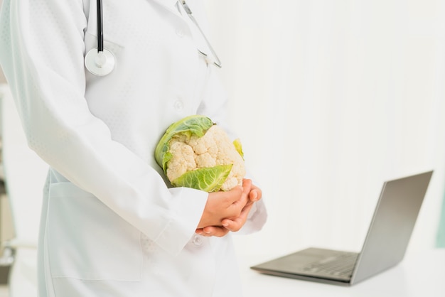 Close-up doctor with cauliflower and laptop