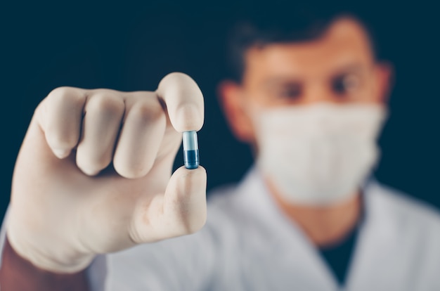 Close-up doctor with mask and gloves holding blue pill with his fingers
