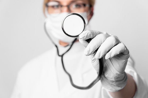 Close-up doctor with surgical mask holding stethoscope