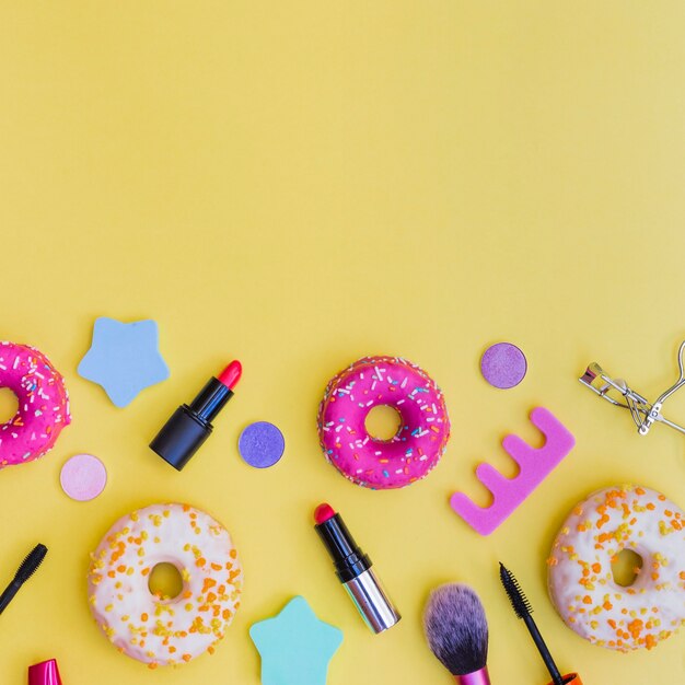 Close-up of donuts; lipstick; eyelash curler; makeup brush and toe divider on yellow background