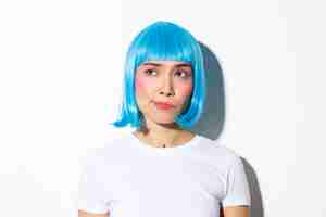 Free photo close-up of doubtful frowning asian girl in blue wig, looking with disbelief at upper left corner, standing.