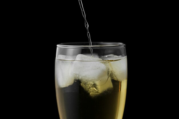 Close-up drink pouring in glass with black background