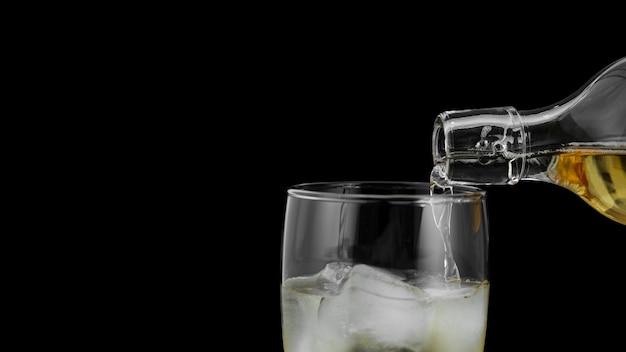 Close-up drink pouring in glass with ice cubes