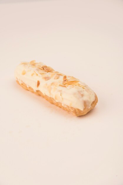 Close up of eclair with white cream and nuts isolated over white