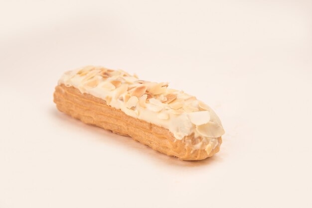 Close up of eclair with white cream and nuts isolated over white