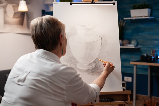 Close up of elderly woman drawing vase on canvas with pencil