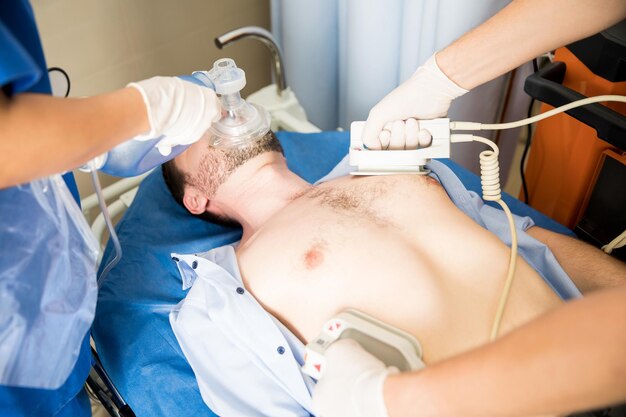 Close up of emergency medical team resuscitating patient with a defibrillator and ambu bag in hospital room