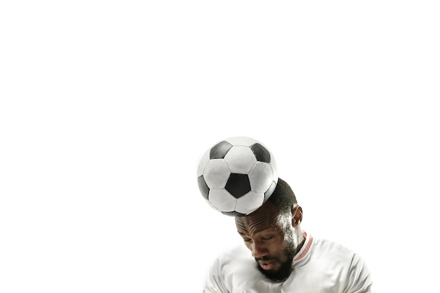 孤立した白い壁に頭でボールを打つサッカーをしている感情的なアフリカ人のクローズアップ。サッカー、スポーツ、顔の表情、人間の感情、健康的なライフスタイルの概念。コピースペース。