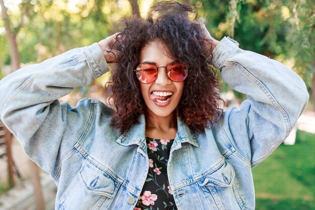 Close up emotional portrait of joyful pretty lady playing with her amazing curly hairs.