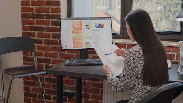 Free photo close up of employee working with charts on papers and computer, doing annual data analysis to plan business project. woman holding files with financial information for development.