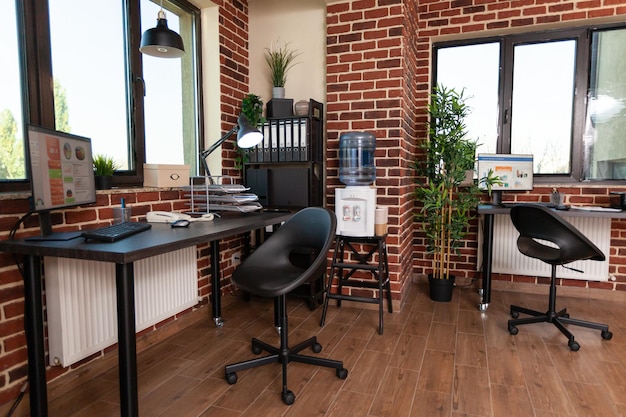 Close up of empty corner with desks in startup office, computer, modern equipment and bookshelf with decor in business space. Workplace with technology and instruments for work.