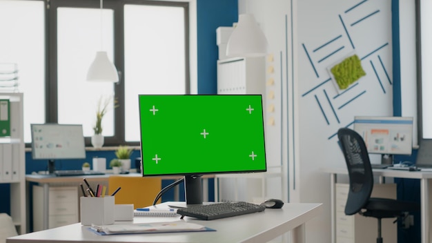 Close up of empty desk with isolated green screen on monitor. Computer with chroma key and mock up template, blank background on display. Chroma-key copy space on digital device.