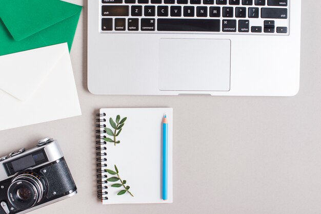 Close-up of envelopes; vintage camera; spiral notepad; colored blue pencil and laptop on gray backdrop