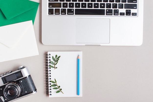 Close-up of envelopes; vintage camera; spiral notepad; colored blue pencil and laptop on gray backdrop