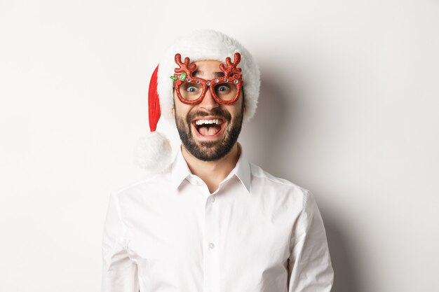 Крупный план возбужденного бородатого мужчины в рождественских очках и шляпе санта-клауса, изумленного промо-предложением, рекламной концепцией зимних праздников