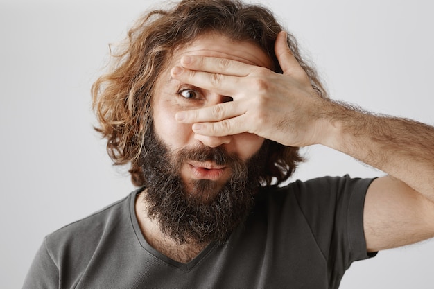 Free photo close-up of excited bearded middle-eastern man peeking through fingers curious