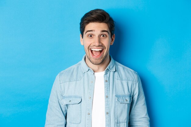 Close-up of excited guy looking at something amazed, standing against blue background for copy space