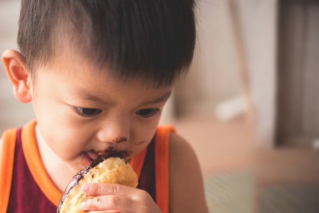 Close up face of hungry little boy eaitng hot donut